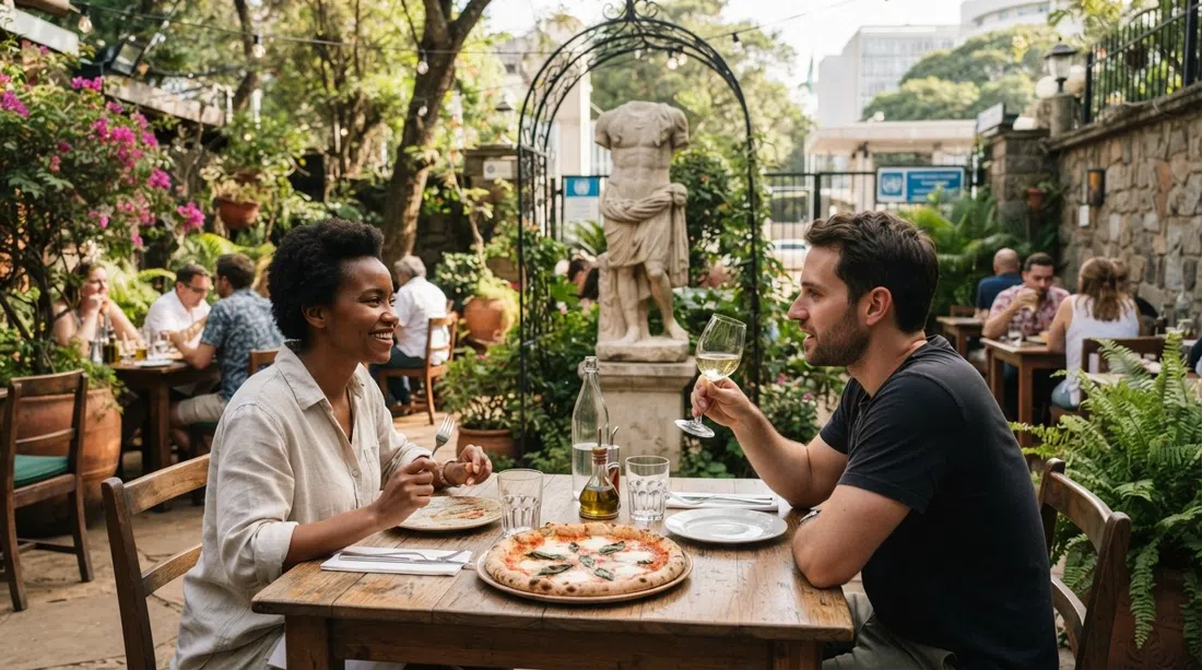 Mesas de jardín de Mediterraneo Ristorante cerca de la entrada de la ONU, con esculturas de estilo romano y una pizza al horno de leña en una mesa informal de almuerzo